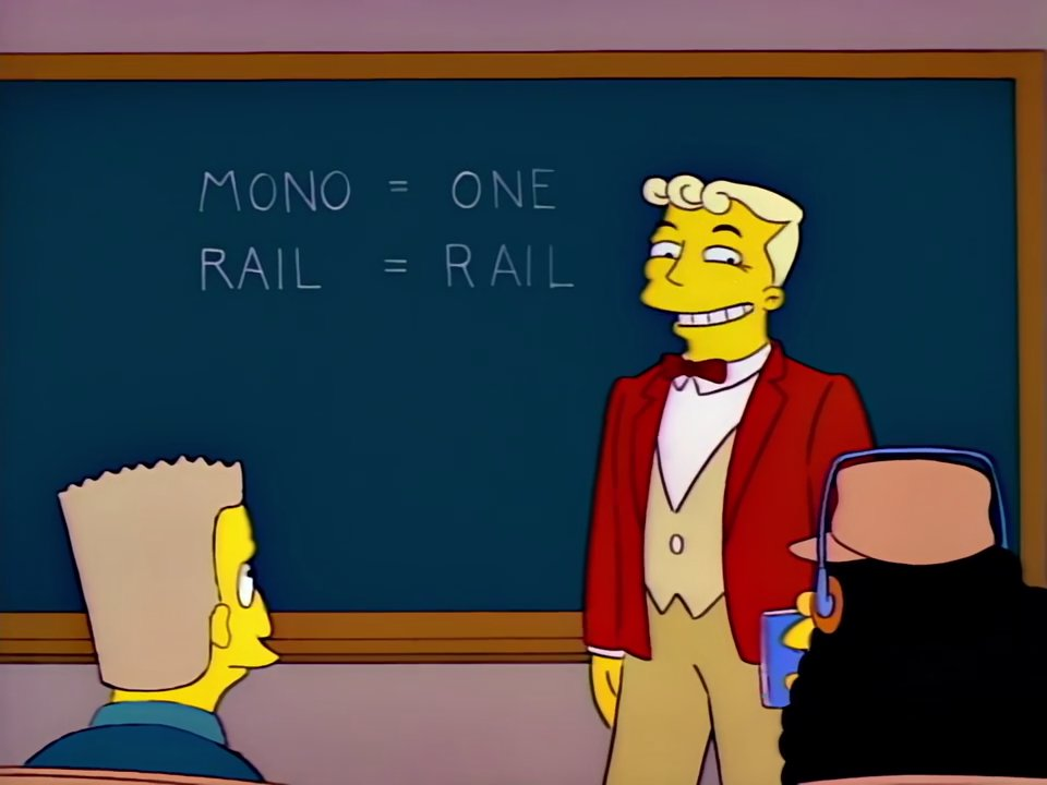 simpsons shot. lyle lanley (a con artist) standing in front of a chalkboard in a classroom. the writing reads, "mono = one. rail = rail." Lyle is smiling coyly in front of a class of people.